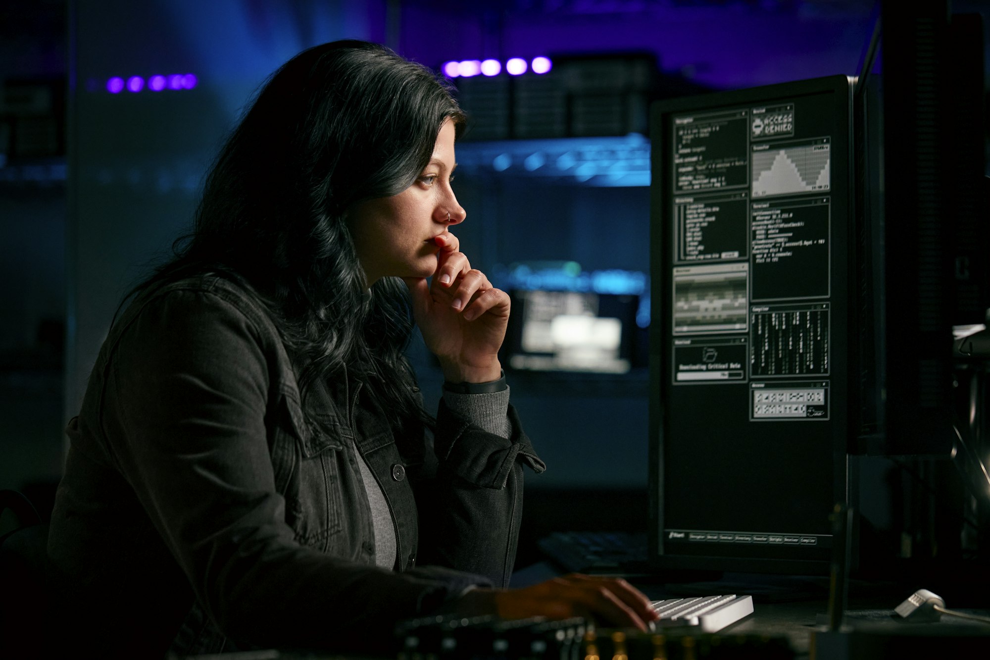 Low Key Lighting Shot Of Female Computer Hacker Sitting In Front Of Screens Breaching Cyber Security